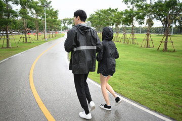 Two friends walk side by side on a rainy park path, enjoying light exercise and fresh air despite wet weather
