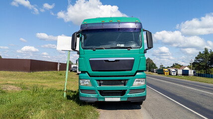 Turquoise semi-truck is parked on the side of the road. The truck is parked on the edge of the road. Close-up of the front of the vehicle.