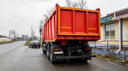 Red dump truck sits on the side of the road near a one-story building. Construction equipment is parked at the edge of the road