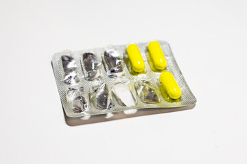 Semi-empty metal blister pack with yellow capsules isolated on white background. Metal blister for capsules