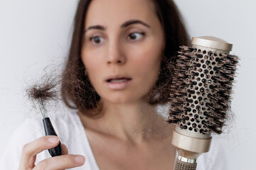 
Worried woman holding hairbrush and clump of fallen hair, suffering from hair loss due to vitamin...