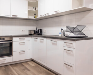 Horizontal wide angle eye level shot of a clean L-shaped kitchen featuring white glossy cupboards, built-in oven, and a wooden floor in a studio © Igor