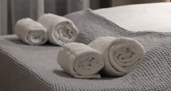 Horizontal wide angle eye level shot focusing on sets of clean, fluffy cotton towels neatly placed on a grey bed runner in a contemporary bedroom