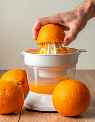 Close-up of a hand squeezing half an orange on a manual citrus juicer. Several whole oranges rest on a wooden surface.The image conveys freshness, healthy living, and homemade juice preparation.