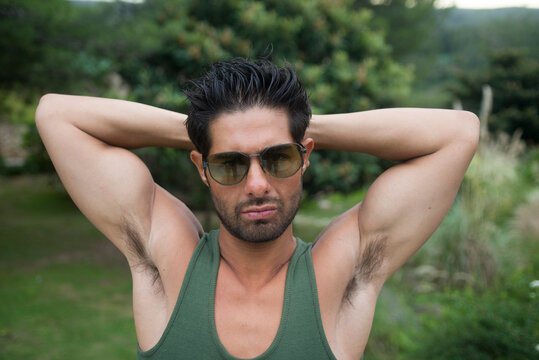Hombre joven latino con anteojos de sol y postura sexy mostrando los musculos de sus brazos