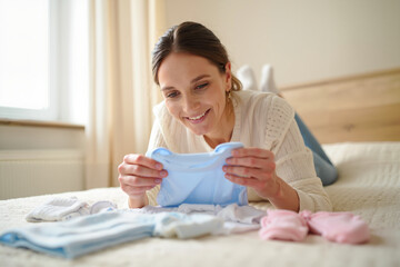 Mother with joyful mood preparing baby clothes against cozy bedroom background