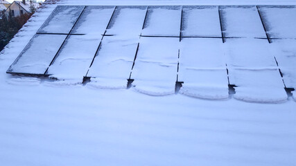 Aerial view of solar panels on the roof of a house covered with snow on a frozen winter day.