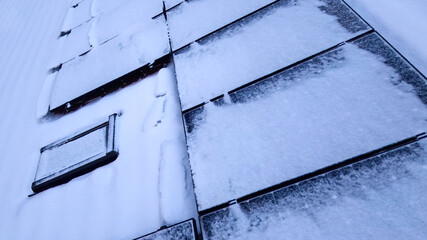 Aerial view of solar panels on the roof of a house covered with snow on a frozen winter day.