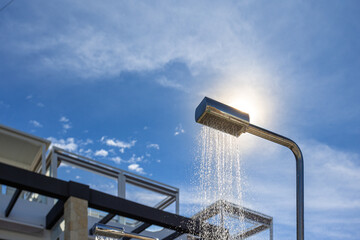 Outdoor shower with running water under blue sky and sunlight near modern building, summer refreshment concept
