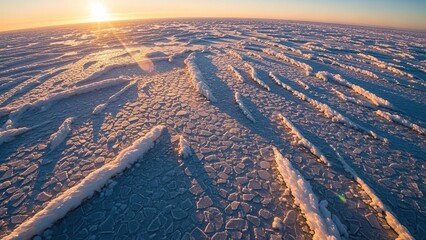 An aerial view of the frozen winter landscape reveals snow-covered mountains and icy water under a cold sky filled with white clouds at sunset