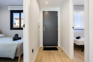 Apartment hallway with front door and two adjacent bedrooms featuring natural light