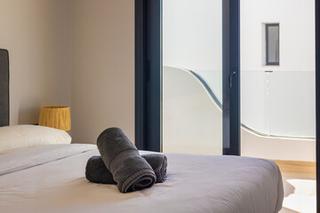 Bright bedroom with balcony access, cozy bed, and neatly folded dark towels