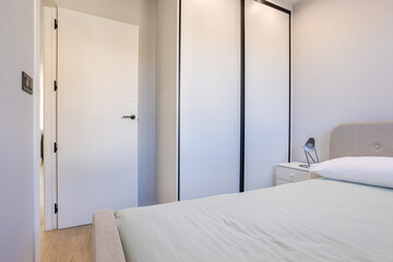 Minimalist bedroom interior with bed, wardrobe, and modern black-accent bedside lamp