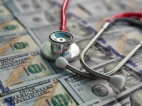 Stethoscope rests on a surface covered with hundred-dollar bills in a clinical - Powered by Adobe