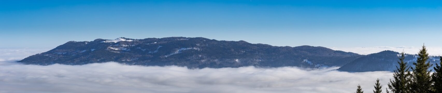 Panoramic view of the Menina Planina plateau rising above a dense thermal inversion layer of white clouds under a clear blue winter sky