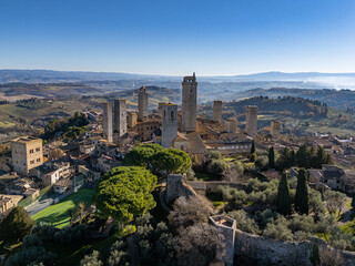 Naklejka premium Aerial view of the medieval walled town of San Gimignano in Tuscany, featuring its iconic stone towers, ancient fortifications, and rolling hill landscape