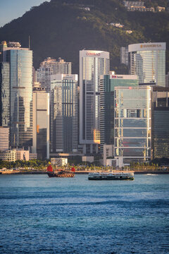 Beautiful day view of an old junk boat and a ferry boat, navigating through Victoria Harbour in front of tall skyscrapers in Hong Kong, SAR, China