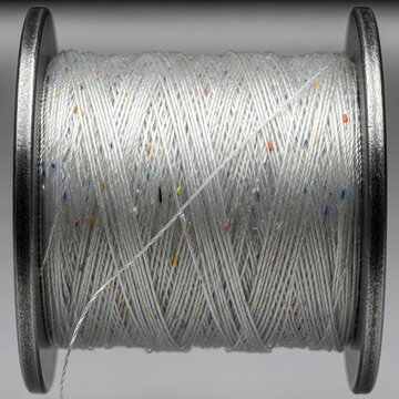 Textured white sewing thread with colorful neps on industrial bobbin, close-up fashion textile