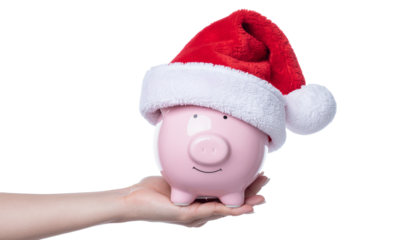 Hand holding a pink piggy bank wearing a red and white santa hat, festive savings concept, holiday finance idea clean white background cutout