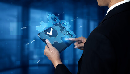 A businessman interacts with a tablet displaying digital gears and a checkmark, symbolizing technology and innovation in a modern office setting. Gantry