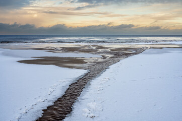Frozen Baltic Sea beach with tidal stream at sunset in Lilaste Latvia