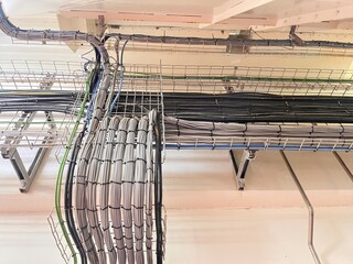 Industrial cable tray system with organized electrical wiring in factory ceiling. Data, power and control cables routed for automation, networking and infrastructure in modern manufacturing plant.