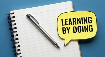 Yellow speech bubble with learning by doing concept rests near a silver pen on a notepad.
