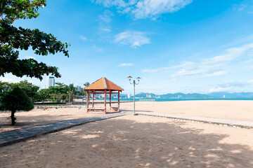 Obraz premium Scenic Tropical Beach in Nha Trang Vietnam Featuring Red Tiled Pavilion and Urban Cityscape under Bright Blue Sky, Wide Angle View with High Contrast. Nha Trang 20.12.2025 Vietnam