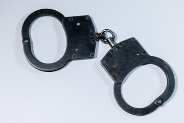 Black metal handcuffs displayed on a clean white background, showcasing the intricate design and functionality of law enforcement equipment in a minimalist setting