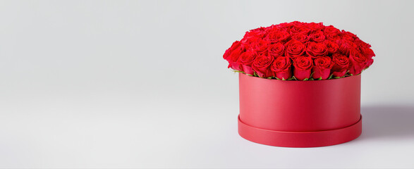 Luxurious bouquet of red roses arranged in a stylish round gift box on the neutral background with area for text or design