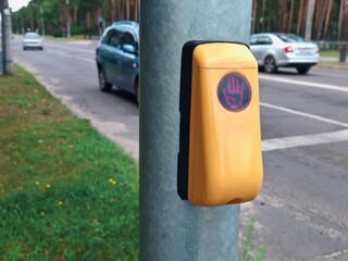 Pressing yellow pedestrian crossing button on metal pole near road. Activating traffic light...