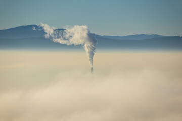 Chimney peeks out of the inversion fog above city Ceske Budejovice. Czech republic