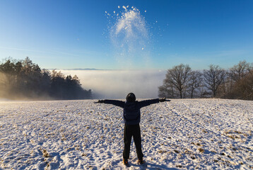 A little boy throws snow into the air on top of small ski slope inversion fog. Sport, touristic Czech landscape background