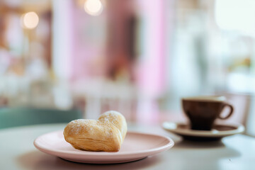 Heart-shaped pastry on a pink plate beside a cup of coffee, creating a cozy cafe atmosphere, perfect for romantic moments and sweet indulgence