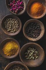 Assortment of colorful spices in wooden bowls arranged on a dark wooden surface, showcasing vibrant textures and natural materials for culinary inspiration and creativity