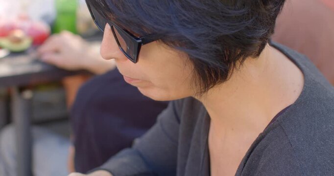 A stylish woman in sunglasses enjoys a meal at a cozy table, savoring dishes like crisp green pepper, in a vibrant outdoor setting