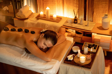 Hot stone massage at spa salon in luxury resort with warm candle light, blissful woman customer...