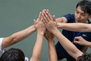 Group of young athletes putting hands together in a huddle. Asian man and teammates showing unity and collaboration on a tennis court. Teamwork concept