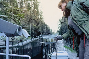 Active ageing concept: adult woman by water infrastructure, observing movement and mechanics around her during a quiet walk, reflecting slow living, curiosity and mindful connection with environment.