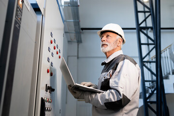 Senior engineer checking industrial control panel using laptop