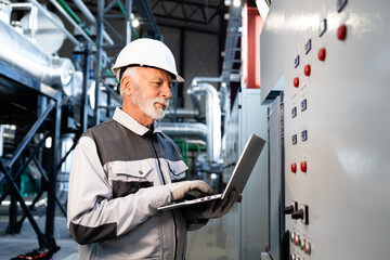 Senior engineer working on laptop in factory control room