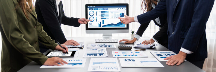 Panorama shot analyst team utilizing BI Fintech to analyze financial report with laptop. Businesspeople analyzing BI data dashboard displayed on laptop screen for business insight. Prodigy