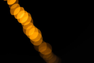 Abstract bokeh lights in orange against a black background. The image features a series of circular light spots creating a soft, blurred effect.