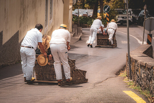 Scenic view of the famous Carreiros do Monte pushing tourists for a thrilling toboggan ride downhill on wicker sleds in Funchal, Madeira, Portugal