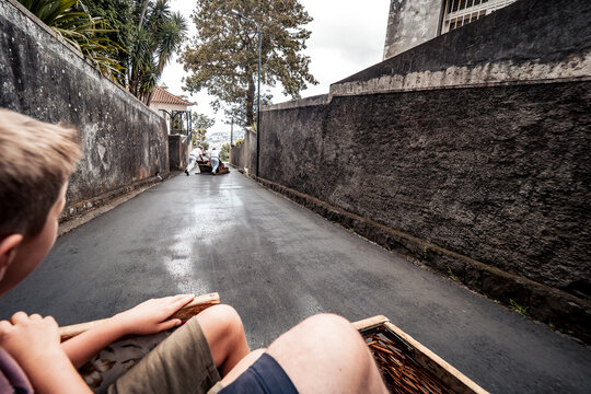 Scenic view of a child enjoying a thrilling toboggan ride downhill on a wicker sled in Funchal, Madeira, Portugal, with the famous Carreiros do Monte