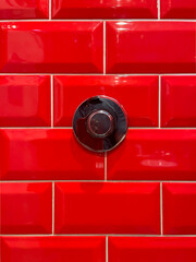 Glossy red ceramic tiles with a chrome metal button centered on the wall, minimalist urban detail with strong color contrast, modern design and geometric pattern background