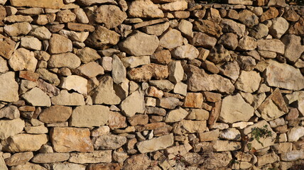 Beige dense wall made of natural stone, part of a fortress or fort as an antique exterior rough background, stonework with antique stylization, full-frame rock material textured background