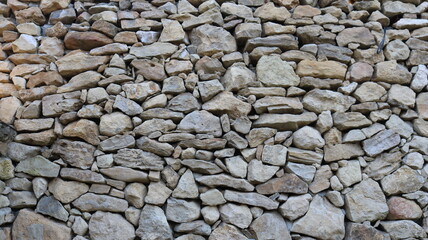 Wall or fence made of solid gray stone laid in a mosaic, fragment of a fortress or fortification structure made of different cobblestones, graphic natural rocky background texture full frame