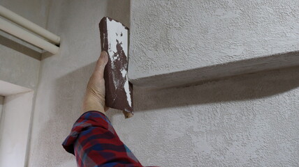 A homemade hand tool for peeling and polishing walls, a piece of sandpaper in the hand of a worker sharpening a convex part of a wall, an emery board in the process of leveling plaster on a wall
