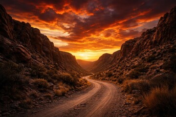 Burning sunset sky over a meandering dirt road enclosed by rocky cliffs with dramatic landscape and clear copy space